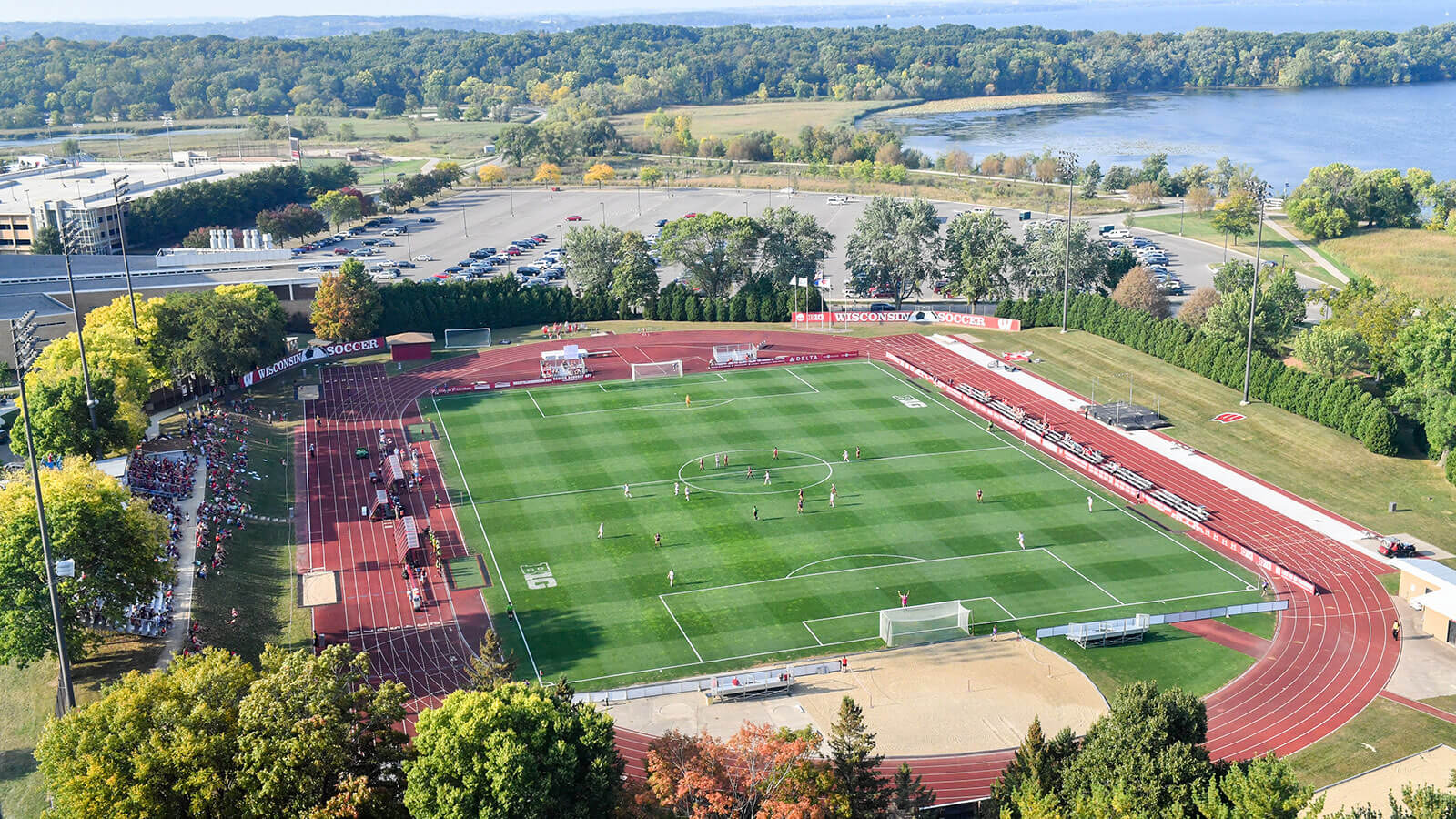 Aerial shot of a green soccer field and a soccer team pro citing, a bright red track surrounds the field.