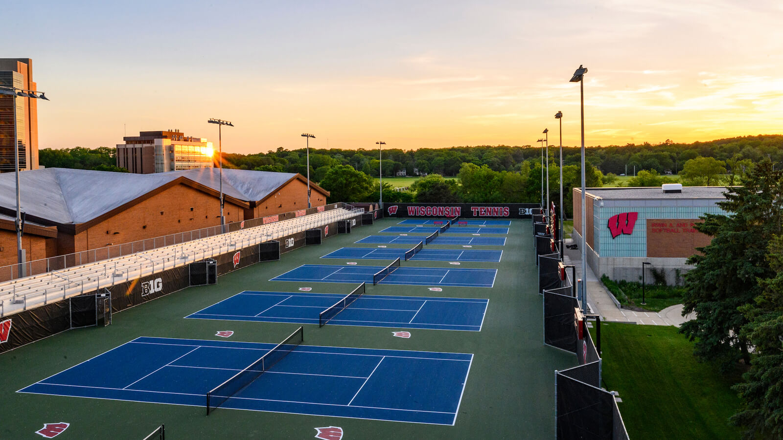 Outdoor long shot of tennis courts and the Nielsen building, trees and woods in the background.