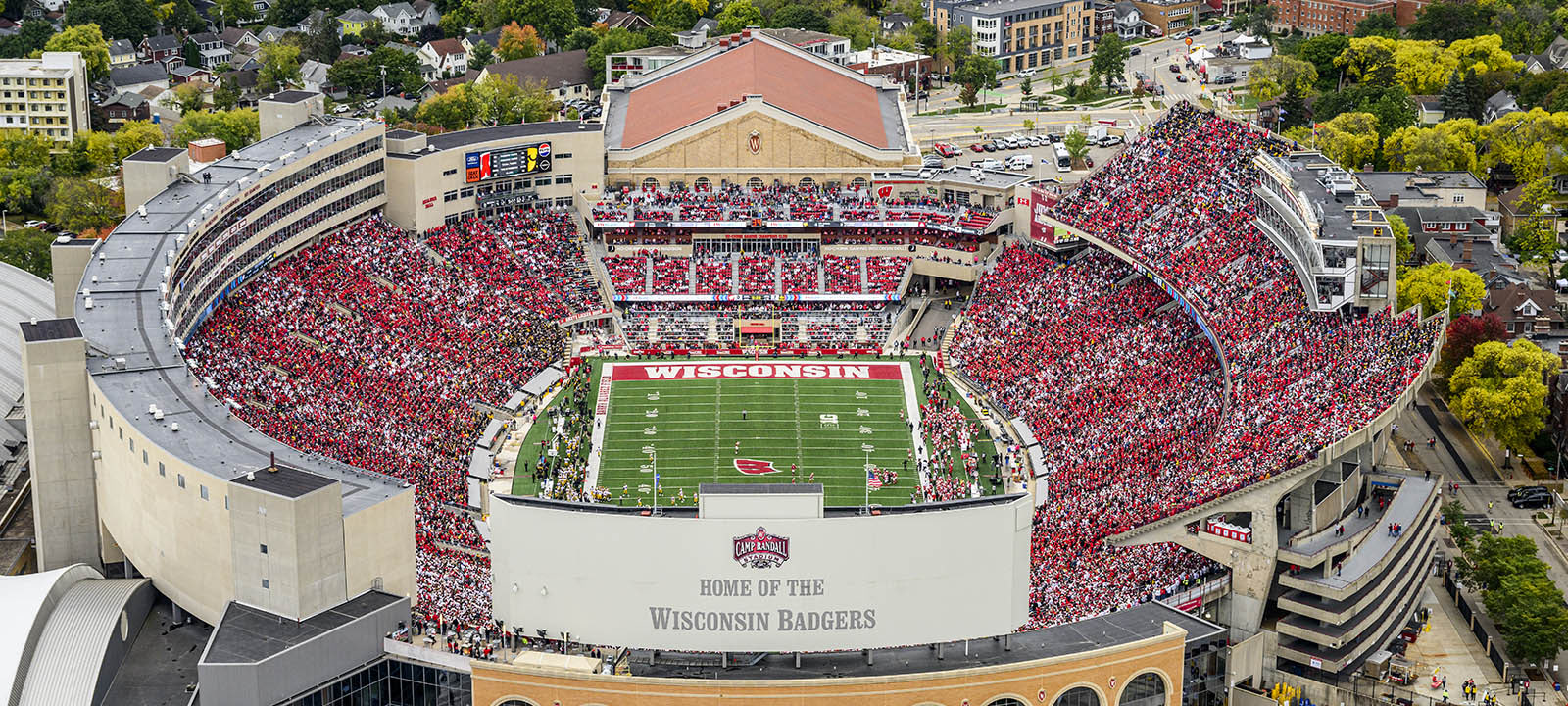 Aerial view of Camp Randall Stadium during a Wisconsin Badgers football game, filled with a packed red- and white-clad crowd.